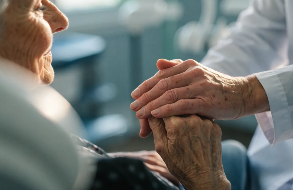 Clinician gently reassuring an older patient by holding their hands