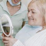a Melbourne patient holding a mirror and admiring her new, natural looking dentures